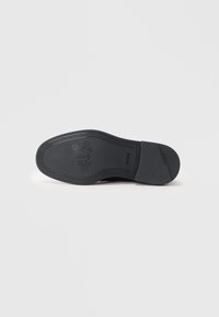 Suola nera di scarpa con una superficie testurizzata, caratterizzata da un logo in rilievo e motivi intricati lungo i bordi. Finitura liscia, design funzionale.
