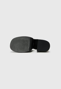 Black sandal with a smooth, rounded toe and a textured sole. The heel is block-shaped and features subtle grooves for grip.
