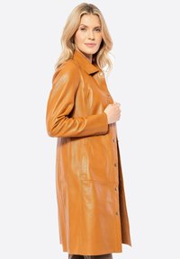 Leren jas in bruin met een rechte snit, drukknopen en zijzakken. Lange mouwen en een kraag benadrukken het moderne ontwerp. Gladde textuur.