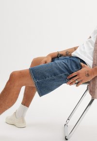 Jeansshorts in Mittblau mit geradem Schnitt, fransenbesäumtem Saum, zwei Seitentaschen und klassischem Fünf-Taschen-Design.