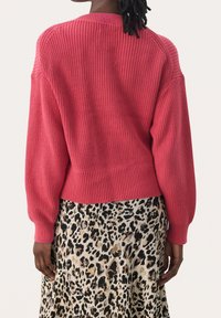 Różowy sweter z dzianiny z prążkowanym dołem i rękawami, w połączeniu z spódnicą w gepardzie wzór. Sweter ma luźny krój i teksturowany materiał.