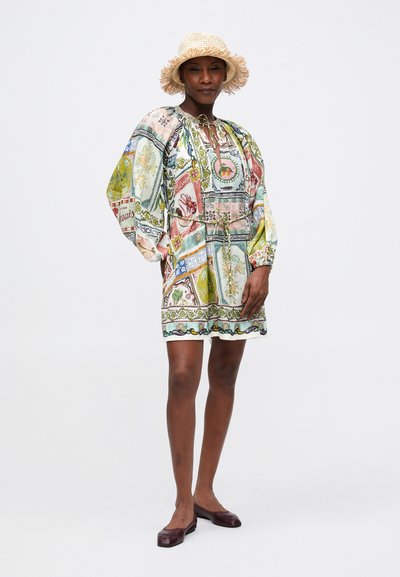 Rochie scurtă colorată, cu mâneci tip balon, guler cu șnur și un design patchwork floral, combinată cu o pălărie din paie împletită și pantofi joși maronii.
