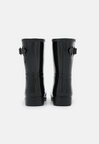Bottes de pluie en caoutchouc noir avec une finition brillante, bout rond et détail de boucle latérale ajustable. Texture lisse, hauteur jusqu'au mollet.