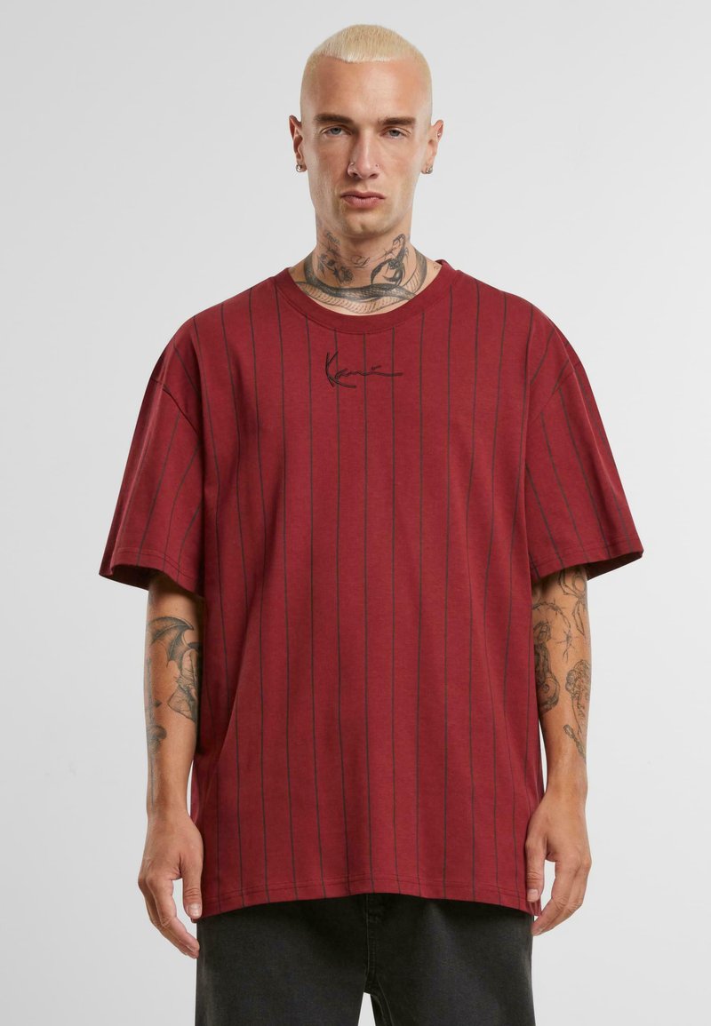 Rødstribet oversized t-shirt lavet af blødt stof, med sorte lodrette striber og et logo i sort på brystet. Korte ærmer.