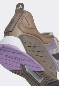 Brun och taupe sneaker med strukturerade element, vit mellansula, lila yttersula och en grå mesh-överdel med tydlig branding och accenter.