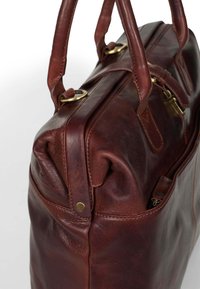 Bruine leren handtas met twee bovenhandvatten, gouden hardware-accenten en een ritsvak. Heeft een gladde textuur en een gestructureerde vorm.
