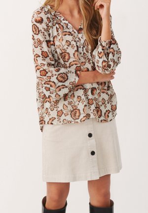 Chemisier à manches longues avec un motif floral en rouille et crème, associé à une jupe en velours côtelé beige comportant trois boutons noirs à l'avant.