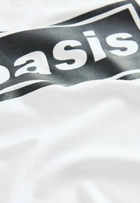 Hvid bomulds t-shirt med sort grafisk print med ordet "basis" og buede linjer, der fremhæver en glat tekstur og moderne design.