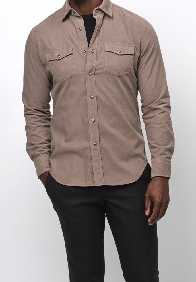 Bruine, lange mouwen, blouse met knopen en twee borstzakken, zilveren knopen en een gestructureerde stof. Gedragen over een zwart shirt, gecombineerd met donkere broeken.