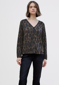 Blusa con estampado de leopardo marrón, escote en V, botones en la parte delantera y mangas largas. Hecha de una tela suave y ligera. Combinada con jeans oscuros.