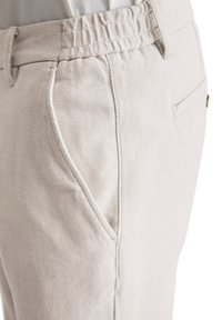 Beige cotton blend trousers with an elastic waistband, featuring a textured surface, side pockets, and a slim cut design.