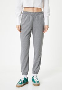 Pantalones de chándal grises con cinturilla y puños elásticos, con una textura suave. Combinados con zapatillas en tonos verde azulado y gris, y calcetines blancos.
