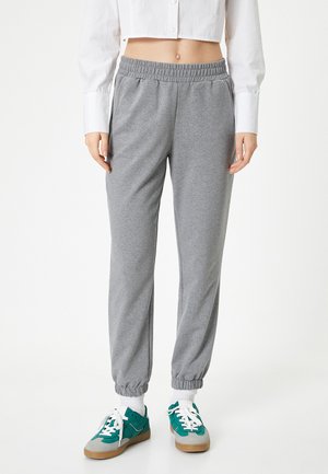 Grijze sweatpants met een elastische tailleband en boorden, voorzien van een zachte textuur. Gepaard met teal- en grijsgekleurde sneakers en witte sokken.