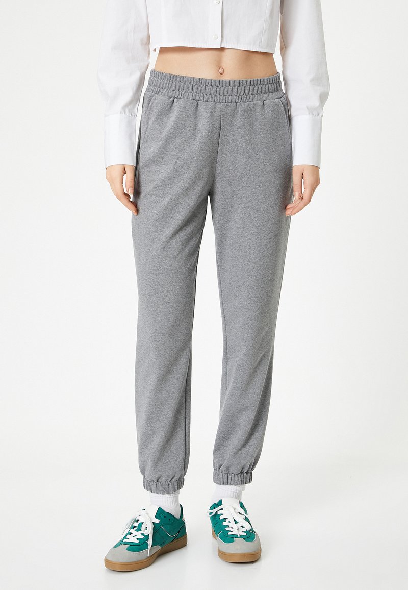 Grijze sweatpants met een elastische tailleband en boorden, voorzien van een zachte textuur. Gepaard met teal- en grijsgekleurde sneakers en witte sokken.