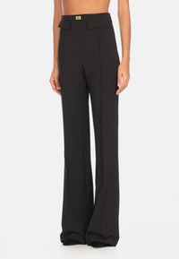 Pantaloni neri su misura con vita alta, gambe svasate e una sottile piega frontale. Presenta un piccolo dettaglio del logo dorato sulla cintura.