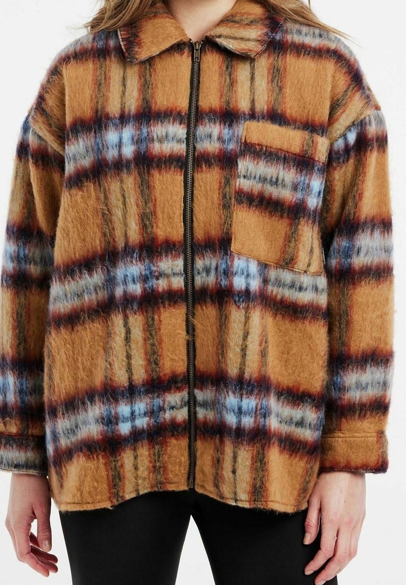 Veste zippée à carreaux marron avec des accents bleus et rouges, fabriquée en matière duveteuse. Comprend un col et une poche poitrine unique.