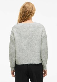 Pull en maille gris clair avec une coupe ample, un motif texturé, des manches surdimensionnées et un ourlet brut. Matériau doux avec une légère duveteux.