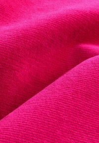 Soe pehme materjal erksas fuksia toonis, millel on tekstuuriga pind, millel on peened sooned ja pehmed voldid, näidates sügavust ja kolmemõõtmelisust.