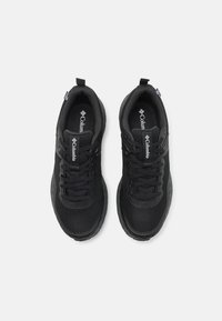 Schwarze Sportschuhe aus Mesh- und synthetischen Materialien, mit runden Schnürsenkeln, Logo-Akzenten und einer strukturierten Gummisohle.