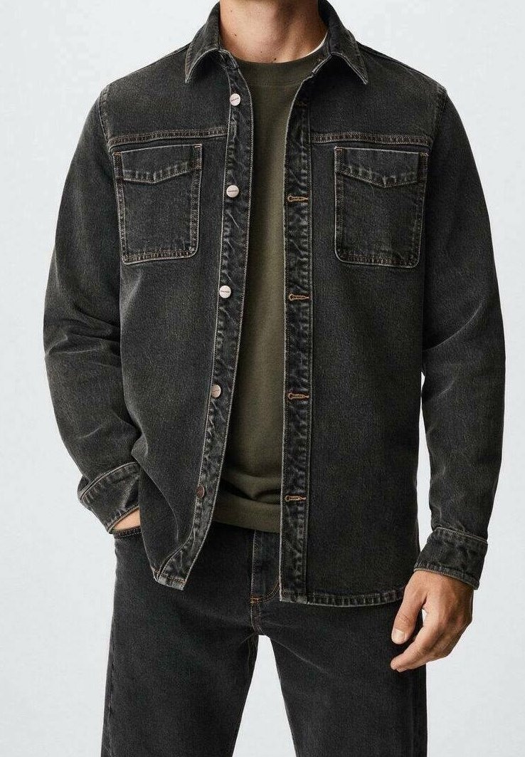 Chaqueta de mezclilla negra con dos bolsillos en el pecho, botones en la parte frontal y un corte relajado, llevada sobre una camisa verde oscura, con detalles de costura visibles.
