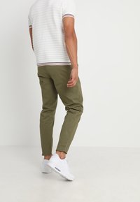 Polo a maniche corte bianco a righe con dettagli rossi e blu marino, abbinato a pantaloni tapered verde oliva e sneakers bianche. Tessuto dal tocco liscio.