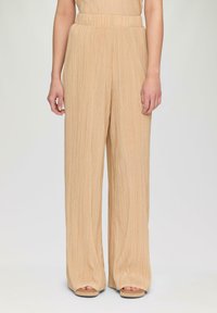 Beige, weite Hosen mit vertikalen Falten, hohem Bund und weichem Textil. Sie haben eine entspannte Passform und enden an den Knöcheln.