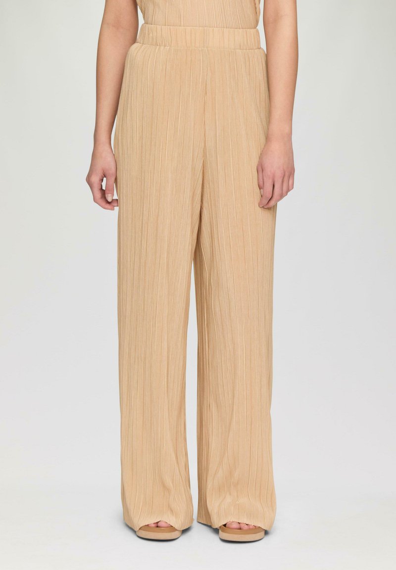 Beige, weite Hosen mit vertikalen Falten, hohem Bund und weichem Textil. Sie haben eine entspannte Passform und enden an den Knöcheln.