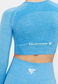 Blå långärmad crop top med ett texturerat mönster och figurnära design. Har en vit "SQUATPROOF" logotyp på baksidan.