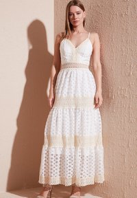 Weißes Maxikleid mit Spitzenakzenten, V-Ausschnitt und dünnen Trägern. Bietet ein gemustertes Textur und einen gestuften Rock mit ausgestellter Silhouette.
