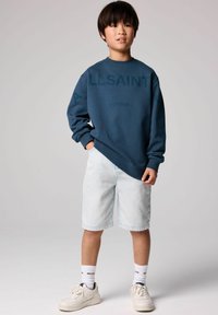 Sudadera de algodón azul marino con el estampado "ALLSAINTS LONDON", combinada con pantalones cortos de mezclilla claros y zapatillas blancas, mostrando un ajuste relajado.