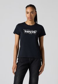 Black cotton t-shirt featuring a white Levi's logo in a sparkly design, short sleeves, and a classic crew neckline. Paired with dark jeans.