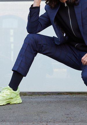 Laivastonsininen ruutukuosinen puku, jossa istuva jakku ja lyhyet housut, yhdistetty kirkkaan keltaisiin tennareihin. Korostaa asua teksturoitu musta neule.