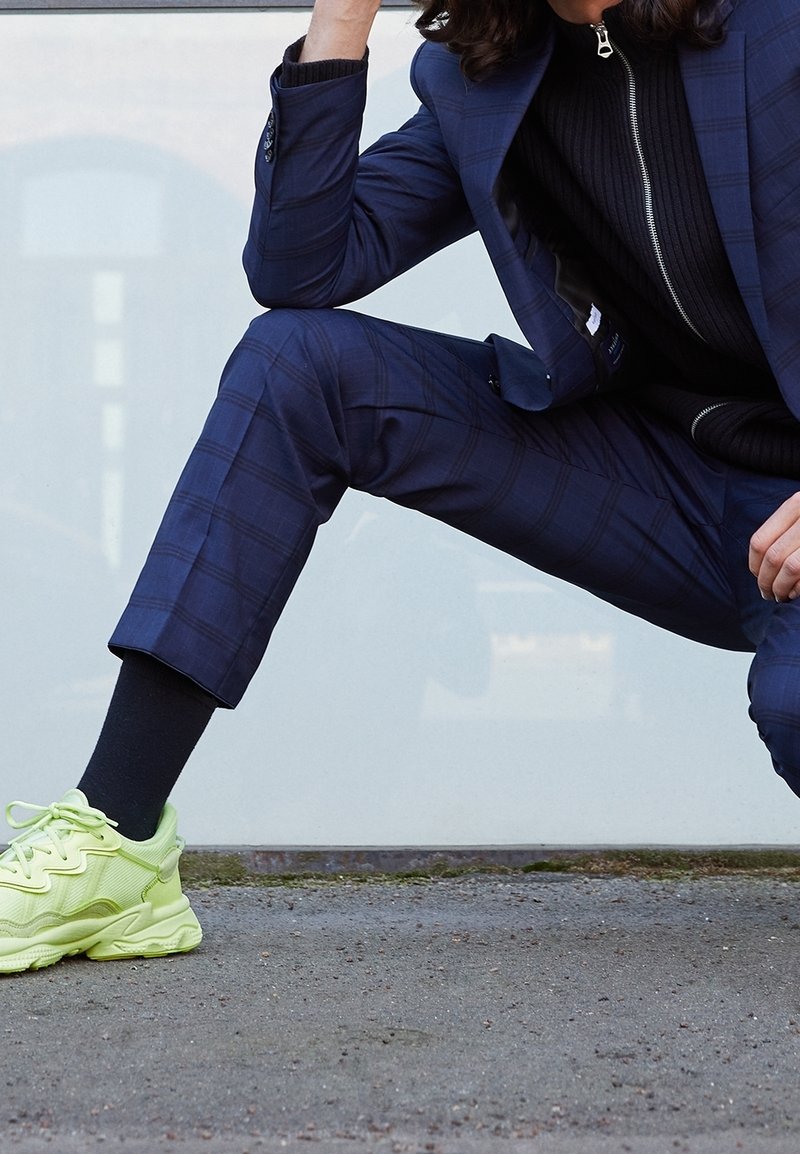 Laivastonsininen ruutukuosinen puku, jossa istuva jakku ja lyhyet housut, yhdistetty kirkkaan keltaisiin tennareihin. Korostaa asua teksturoitu musta neule.