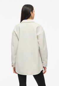 Φωτεινό γκρι oversized σακάκι με γιακά, μακρ�ιά μανίκια και κουμπωτές μανσέτες. Λείος υφασμάτινος χαρακτήρας και στρογγυλή γραμμή στρεβλωγίας με πλαϊνές σχισμές.