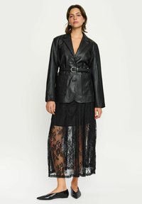 Mustast nahast pintsak, mis on istuv ja varustatud vööga, koos läbipaistva musta pitsseelikuga ning mustade teravate kannatustega.