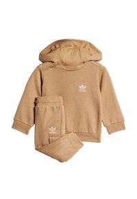Brūnas kapuci jaka un saskaņota bikses, kas izgatavotas no mīksta materiāla, ar baltu adidas logotipu uz krūtīm un sānos.