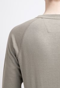 Grijze langharige shirt met een geribbeld patroon en raglanmouwen, met een subtiele naaddetail langs de schouder.
