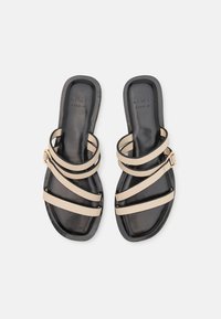 Sandale negre cu barete bej, având o talpă plată și un accent cu cataramă aurie. Textură netedă, design minimalist, stil cu vârful deschis.