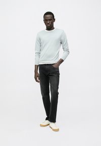 Φωτεινό γκρι, πουλόβερ με μακριά μανίκια, συνδυασμένο με μαύρα τζιν και λευκά αθλητικά παπούτσια. Το πουλόβερ έχει στρογγυλή λαιμόκοψη με λευκή λεπτομέρεια.