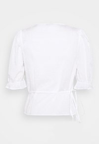 Blouse blanche avec un motif à pois texturé, manches bouffantes et taille ceinturée. Dotée d'un col rond et d'une silhouette légèrement ajustée.