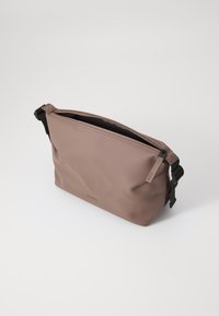 Sac à épaule marron imperméable avec fermeture éclair, sangle noire réglable, texture lisse et logo de la marque en relief sur le devant.