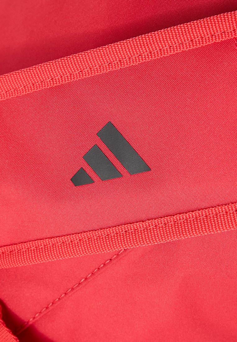 Tela roja con una textura suave que presenta un logo negro de Adidas en un diseño triangular. Los bordes están reforzados con costuras de contraste.
