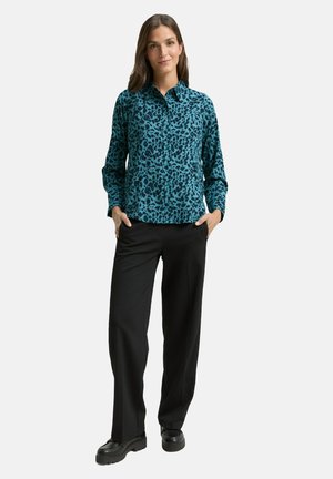 Blaues Hemd mit Leopardenmuster und Knöpfen, lange Ärmel, schwarze Hose und klobige schwarze Schuhe. Glatter Stoff und maßgeschneiderte Passform.