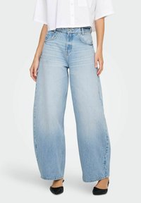 Heledad sinine lai lõige teksad, mis on valmistatud denimist, kõrge vöökoha, kulunud tekstuuri ja viie tasku kujundusega, kombineeritud valge särgiga.