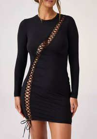 Czarna sukienka z długim rękawem z diagonalnym wycięciem z detalami sznurowania. Wykonana z elastycznego materiału z dopasowanym krojem.