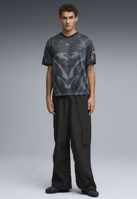 Maglietta sportiva nera con scollo a V, decorata con motivi metallici, abbinata a pantaloni cargo neri larghi e scarpe da ginnastica con texture.