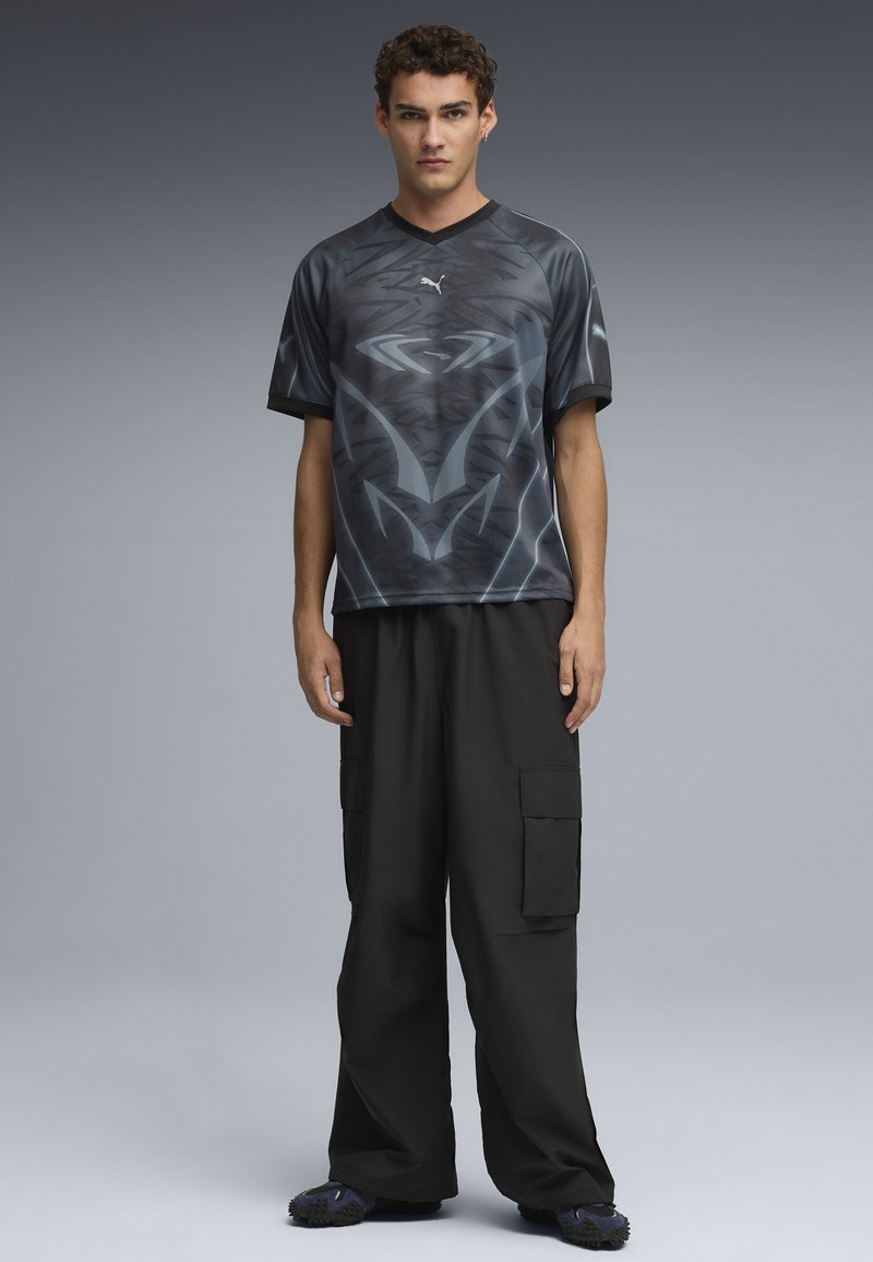 Maglietta sportiva nera con scollo a V, decorata con motivi metallici, abbinata a pantaloni cargo neri larghi e scarpe da ginnastica con texture.