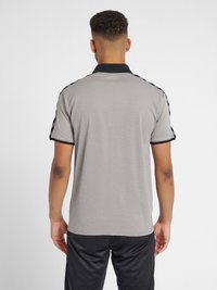 Polo grigio con colletto nero, caratterizzato da strisce nere lungo le spalle. Il tessuto sembra strutturato e la vestibilità è regolare.