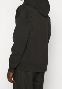 Černá mikina s kapucí, s texturovanými ramenními panely, žebrovanými manžetami a lemem, s uvolněným střihem a hladkým materiálem.
