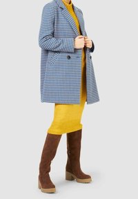 Modrý a bílý kostkovaný vlněný kabát s klopy s výřezy, žluté pletené šaty a hnědé kozačky nad kolena s robustními podpatky a detailním zipem.